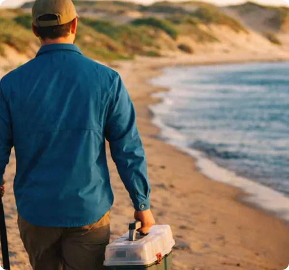 Angler carrying gear box while walking along water shoreline canvas scene